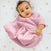A baby rests on a white blanket with pink polka dots in a pink HALO Easy Transition SleepSack TOG 1.5. Their gently curled hair complements their curious gaze, while the onesies 3-layer design ensures warmth and comfort, promising your little one better sleep.