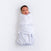 A baby is comfortably wrapped in a HALO Swaddle 100% Cotton TOG 1.5 with adjustable wings, featuring a white blanket with blue stars. Resting on a light surface, the babys face is visible, looking upward while promoting healthy hip development.