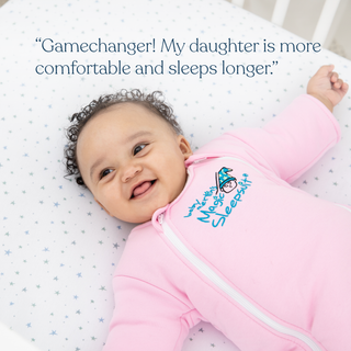 A smiling baby in a pink onesie lies on a star-patterned crib sheet. Text above: “Gamechanger! HALO Baby Merlins Magic Sleepsuit® 100% Cotton kept my daughter comfy and helped her sleep longer—even during sleep regression.”.