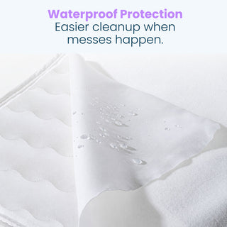 A white waterproof cover for the Essential Breathable Crib Mattress with a corner folded back, showing water droplets beaded on the surface beneath the text: Waterproof Protection. Easier cleanup when messes happen.