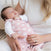 A baby peacefully sleeps wrapped in a HALO Swaddle Micro-Fleece TOG 3.0, cradled by a woman in a white sweater. Her ring is visible as her hand gently rests on the baby, who benefits from healthy hip development thanks to the cozy embrace of their swaddle.