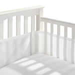 Close-up of a white crib corner showing vertical slats with a HALO Breathable Mesh Crib Liner for Mini Crib. Its minimalist design ensures safety, casting soft shadows on the infant bedding and liners.