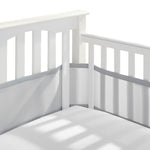 Close-up of a white baby crib corner with slatted sides, featuring the HALO Breathable Mesh Crib Liner for Full Sized Crib in light gray. The mattress, under a white sheet, lies serenely beneath soft shadows.