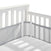 Close-up of a white baby crib corner with slatted sides, featuring the HALO Breathable Mesh Crib Liner for Full Sized Crib in light gray. The mattress, under a white sheet, lies serenely beneath soft shadows.