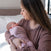 A woman with long brown hair cradles her swaddled newborn as they gaze at each other, both dressed in matching mauve HALO Swaddle SuperSoft Bamboo TOG 2.0 outfits in a bright, cozy bedroom.