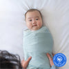 A baby in a light blue HALO SleepSack Bamboo Swaddle Bundle lies on a white bed as adult hands gently hold them. The Best of BabyCenter 2025 Award Winner badge appears in the lower right corner.