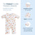 The HALO Disney® Winnie the Pooh Baby Merlin’s Magic Sleepsuit® 100% Cotton is displayed, featuring a white design adorned with colorful Winnie the Pooh prints. Details include a gently scooped neckline, zipper covers, and open hands and feet to promote self-soothing and grasping—perfect for babies transitioning from swaddling. The product emphasizes healthy sleep habits inspired by the original Magic Sleepsuit approach.