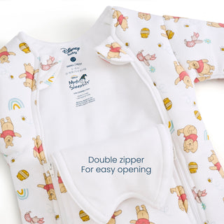 Close-up of the Disney® Winnie the Pooh Baby Merlin’s Magic Sleepsuit® 100% Cotton by HALO, featuring adorable prints of Winnie the Pooh and friends with rainbows and honey pots. This sleepsuit is perfect for transitioning from swaddling, providing comfort as your baby adjusts. The suit includes a convenient double zipper for easy opening, as highlighted by the open flap labeled “Double zipper for easy opening.”.