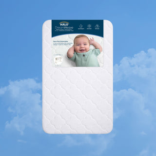 Rectangular white HALO Bedside Sleeper DreamWeave Breathable Pad with a scalloped pattern, featuring a product label showing a smiling baby and icons for the pad’s hypoallergenic and washable features.