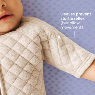 A baby wearing a HALO Easy Transition SleepSack TOG 1.5, a quilted sleep sack with sleeves that prevent the startle reflex while allowing movement for an easy transition.
