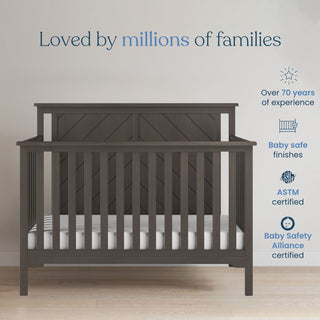 A Hampton Flat Top 4-in-1 Convertible Crib in Dapper Gray by Child Craft is centered in a bright room. Above, text reads “Loved by millions of families.” Icons highlight 70+ years experience, baby-safe finishes, ASTM certification, and adjustable support.