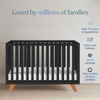 The Child Craft Soho 4-in-1 Convertible Crib in Ebony with wooden legs stands on a light wood floor. Baby safe finishes, ASTM certified, converts to a toddler bed, and is loved by millions of families.