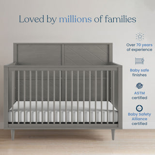 A Surrey Hill 4-in-1 Convertible Crib by Child Craft in Lunar Gray with a white mattress stands against a pale wall. Above, text reads Loved by millions of families, with icons for 70+ years' experience and trusted certification.
