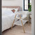 A woman sleeps in bed next to the HALO BassiNest® Essential Sleeper, a modern space-saving bassinet that's empty. The room has light wood floors, a plant, and a window with black frames.