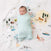 A baby peacefully sleeps, wrapped in an aden + anais boutique 100% cotton muslin swaddle. The breathable fabric gently surrounds the baby on a map-themed blanket, featuring animals, trees, and landmarks that create a whimsical scene.