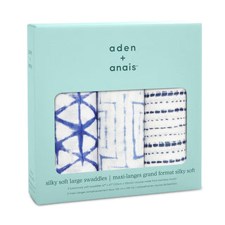 A teal box holds three aden + anais boutique silky soft swaddle blankets. Crafted from bamboo-infused viscose, these large white swaddles showcase blue geometric and dotted designs, with the packaging emphasizing their generous size and luxurious material.