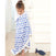 A young girl stands on a staircase wrapped in an aden + anais boutique silky soft muslin dream blanket. She looks down with a small blue toy fish beside her. The setting feels bright and airy, enhancing the cozy atmosphere.