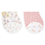 The aden + anais organic cotton muslin burpy bibs 2 pack showcases two GOTS-certified bibs. One features a floral and butterfly pattern on white, while the other has a white floral design on pink. Both offer rounded bottoms with an extra fabric fold for added convenience.