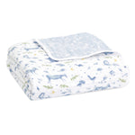 The aden + anais organic cotton dream blanket is GOTS certified and features soft white cotton muslin with blue deer and bird prints, green leaf patterns, and a corner fold revealing a contrasting blue design.