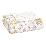 Aden + anais organic cotton dream blanket features a folded design with floral patterns of yellow and pink flowers, green leaves, and butterflies on a white background. Made from soft cotton muslin fabric, its layered to highlight texture and is GOTS certified for peace of mind.