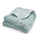The aden + anais organic cotton muslin dream blanket is a neatly folded, soft, green baby blanket featuring a subtle boat pattern. GOTS certified, it includes a decorative striped trim on one edge.