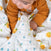 A baby in an orange ribbed outfit crawls on a white aden + anais Organic Baby Essentials Bundle blanket, featuring colorful fruit patterns like lemons and blue polka dots, creating a cozy and cheerful scene.
