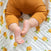 A baby wearing orange ribbed pants relaxes on an aden + anais Organic Baby Essentials Bundle Dream Blanket, showcasing a white and yellow lemon pattern, with their legs and bare feet in view.