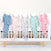 Five aden + anais snuggle knit™ newborn gift set sleep gowns in blue, white with red, gray, green, and pink adorn a white crib with wooden legs. This ensemble is perfect as a newborn gift and is set against a plain light background.