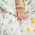 A child in a textured beige long-sleeve shirt gently grips an aden + anais organic cotton muslin swaddle blanket from a 4-pack, adorned with blueberries and lemons.