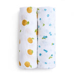 Aden + Anais organic cotton muslin swaddle blanket 2 pack, GOTS certified, includes two rolled blankets. One has an orange fruit print with green leaves, and the other features blue fruit-like patterns with green leaves, set side by side on a plain white background.