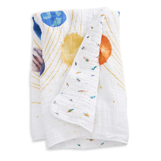 The aden + anais organic cotton muslin dream blanket is a soft white baby blanket with a vibrant solar system design on one side and rockets, planets, and stars on the reverse—ideal for cozy crib bedding.