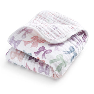 The aden + anais organic cotton muslin dream blanket is shown folded, featuring a white background with pastel bows in pink, purple, and green—perfect for crib bedding.