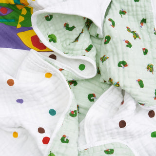 A close-up of the aden + anais essentials cotton muslin dream blanket, crumpled and cozy, shows colorful polka dots and Very Hungry Caterpillar illustrations on a light green background.