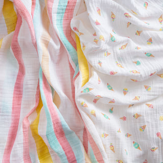 The aden + anais essentials cotton muslin swaddle blanket 2 pack includes one white blanket with pastel stripes in pink, blue, yellow, and orange, and another featuring colorful ice cream cones.