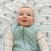 A smiling baby with blue eyes and rosy cheeks lies on the aden + anais essentials cotton muslin swaddle blanket, featuring a light butterfly pattern. The soft, breathable 4-pack makes naptime cozy and comfortable.