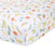 A close-up of the white aden + anais essentials cotton muslin crib sheet reveals a playful print with colorful fruits and vegetables like bananas, carrots, peas, and apples, adding a bright and whimsical touch to the bedding.