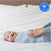 A smiling baby lies in a SuperSoft Bamboo Swaddle TOG 2.0 by HALO on a white bed as an adult adjusts the wrap. A 