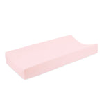 A pale pink, rectangular changing pad cover by aden + anais, designed for a babys changing table with raised edges on two sides. It features essentials cotton muslin, offering a smooth and slightly cushioned surface for added comfort.