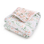 The aden + anais essentials cotton muslin dream blanket is depicted folded, showcasing a pink floral top with white flowers and green leaves, while the underside flaunts a similar design on white—ideal for snuggling.