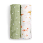 Two aden + anais essentials cotton muslin swaddle blankets are rolled side by side: one green with white arrows, the other breathable with colorful animal and nature designs, including a deer, fox, and trees.