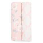 The image shows two rolled swaddle blankets from the aden + anais essentials silky soft swaddle blanket 2 pack. The pink one features a floral pattern, while the white one has a pink geometric design. Made from bamboo-infused viscose, they are perfect for sensitive skin and neatly displayed side by side.