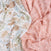 A close-up of aden + anais essentials silky soft swaddle blanket 2 pack shows a bamboo-infused floral pattern on white, and a pink geometric design. Both fabrics are softly draped, highlighting their gentle folds and textures, perfect for babys sensitive skin.