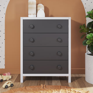 The Child Craft Orbit 4 Drawer Chest in Ebony/Matte White features large round knobs and stands on a wooden floor. Decorative vases sit on top, with plants and children's toys nearby against a brown and white wall.