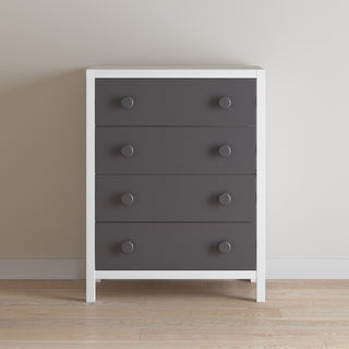 The Child Craft Orbit 4 Drawer Chest in Ebony/Matte White, featuring a modern white frame and four dark drawers with large round knobs, stands on a light wood floor against a plain beige wall.