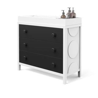 A sleek Child Craft dresser in black and white with three drawers and round accents, topped with the F01792 Universal Changing Table Topper in Lunar Gray—ideal for organizing baby essentials with style.