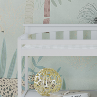 A close-up of the Child Craft Flat Top Baby Changing Table in matte white, featuring baby-safe finishes, a decorative gold sphere and book on the lower shelf, against pastel botanical wallpaper—ideal nursery storage.