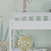 A close-up of the Child Craft Flat Top Baby Changing Table in matte white, featuring baby-safe finishes, a decorative gold sphere and book on the lower shelf, against pastel botanical wallpaper—ideal nursery storage.