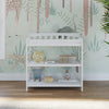 The Child Craft Flat Top Baby Changing Table in matte white, featuring three shelves with baby-safe finishes, provides nursery storage beneath a pastel safari animal mural with giraffes, ostrich, and cheetah. Sunlight shines on the wooden floor.