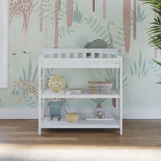The Child Craft Flat Top Baby Changing Table in matte white, featuring three shelves with baby-safe finishes, provides nursery storage beneath a pastel safari animal mural with giraffes, ostrich, and cheetah. Sunlight shines on the wooden floor.