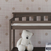 A white teddy bear sits on the lower shelf of the Child Craft Flat Top Baby Changing Table in Dapper Gray, placed against a pink polka-dot wallpapered wall with a stack of books visible in the lower right corner.
